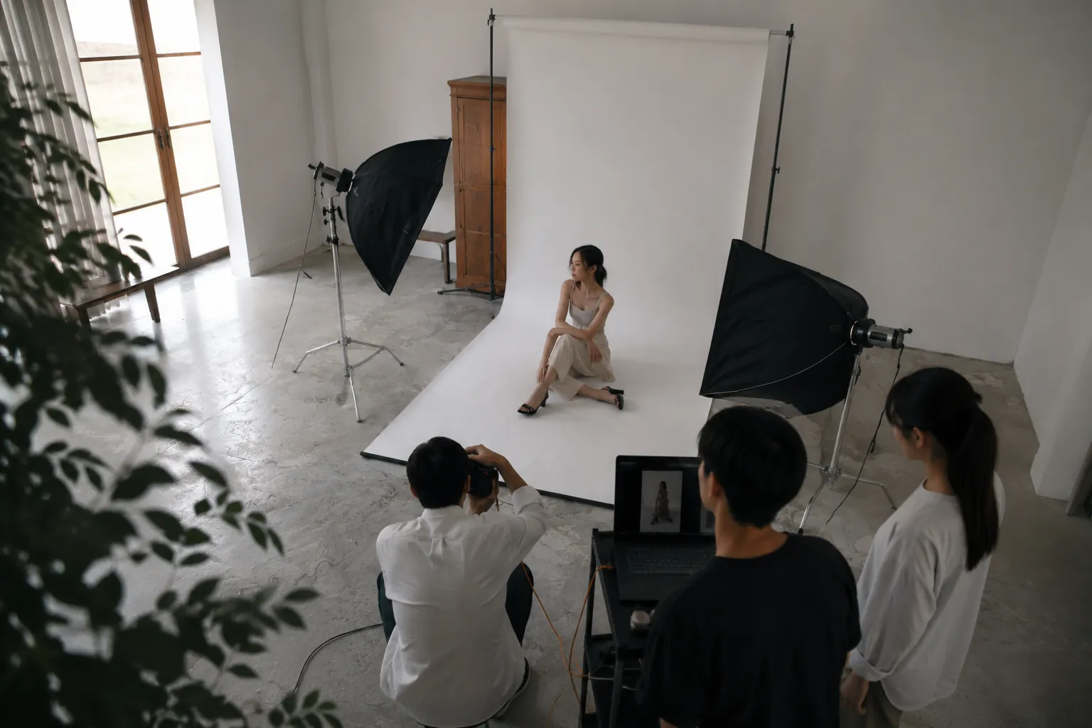 アパレル商品の撮影スタジオでモデル撮影中、カメラマンとアシスタントが画面確認している様子(イメージ)